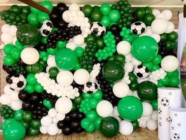 Green, white, and black balloon wall with soccer ball balloons.