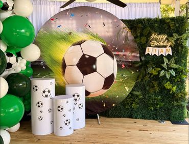 Soccer-themed birthday setup with green and white balloons and a large soccer ball backdrop.