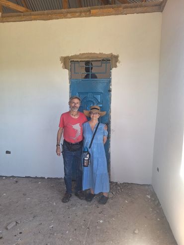 A couple stands inside a room with unfinished walls and a blue door.