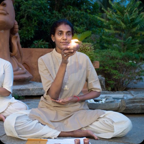 Woman in traditional attire holding a lit clay lamp during a serene outdoor ritual.