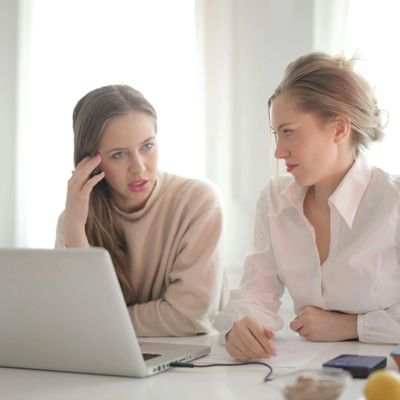 Two women engaged in a serious discussion while looking at a laptop.