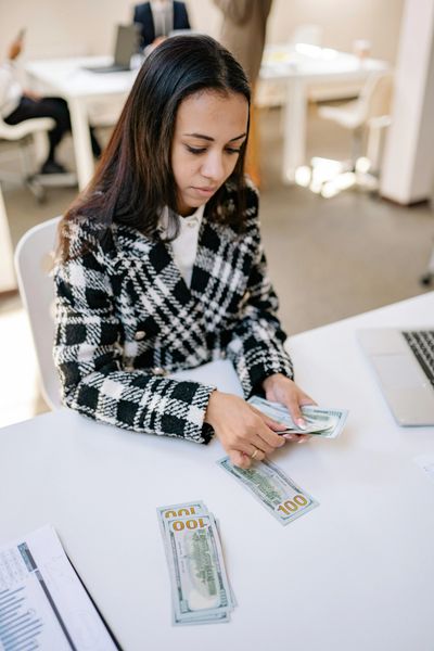 A woman counting US dollar bills at a desk in an office.