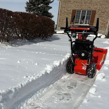 Red snow blower clearing a driveway covered in fresh snow.