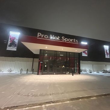 Entrance of Pro Net Sports building at night with snow on the ground.