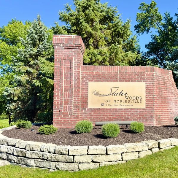 Entrance sign for Slater Woods of Noblesville with greenery and blue sky.