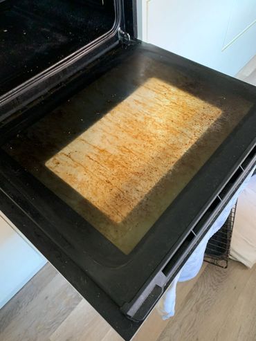 Oven door with a dirty glass window showing grease stains.
