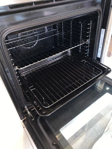 Open black oven with racks and baking tray inside.