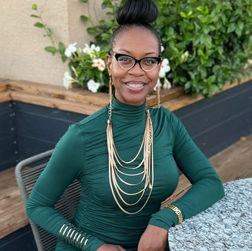 A woman in a green dress sitting at a table outdoors, smiling.
