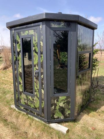 Small camouflage-patterned guard booth with glass windows in a grassy area.