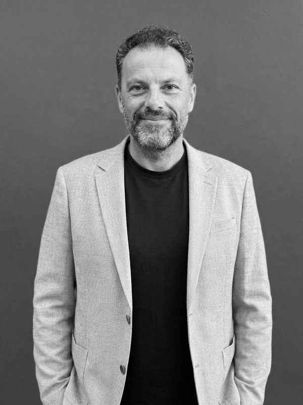 Man with beard wearing light blazer and black shirt smiling.
