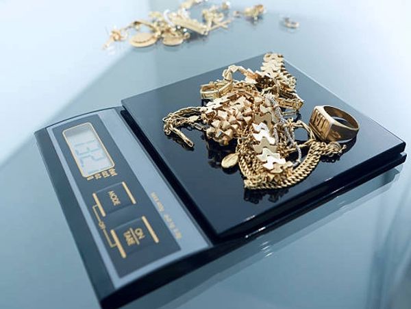 Gold jewelry being weighed on a digital scale showing 122 grams.