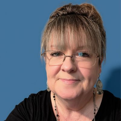 Smiling woman with glasses and earrings against a blue background.