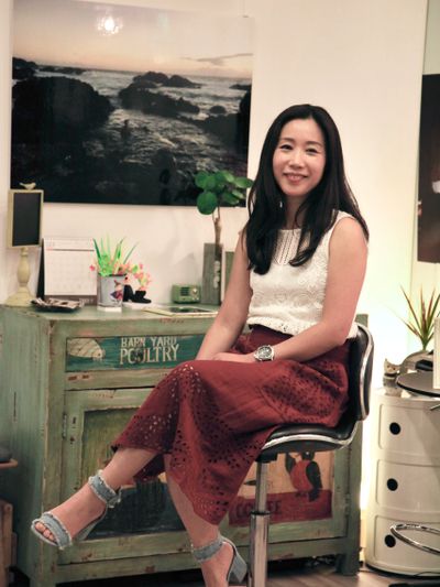 A smiling woman sitting on a swivel chair in a cozy, vintage room.