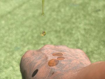 A dropper releasing golden oil onto a tattooed hand outdoors.