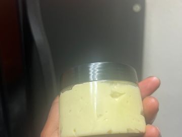 Hand holding a small jar of yellow cream or lotion.