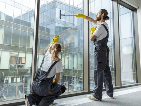 Two people cleaning a window in a commercial building