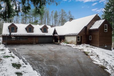 Snow-covered driveway and log cabin in forest.