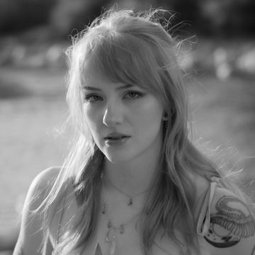 Black and white portrait of a woman with long hair and a tattoo on her shoulder.