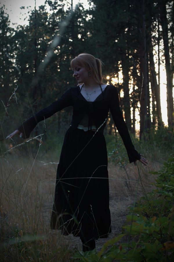 Woman in black dress dancing in the forest at dusk.