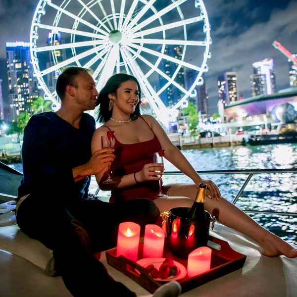 Couple enjoying a romantic night on a boat with city lights and a ferris wheel behind.