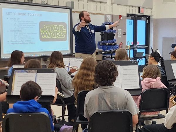 A band conductor leads students practicing Star Wars music in a classroom.