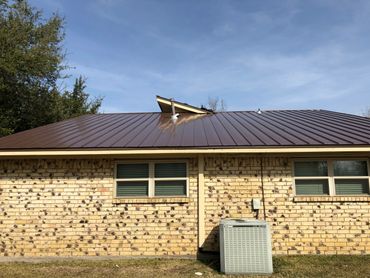 A residential house with a damaged metal roof under a clear sky.