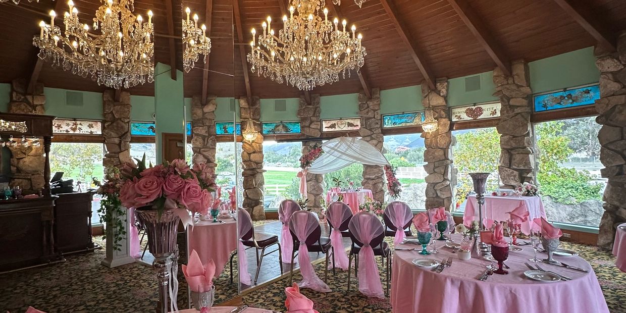 Elegant wedding reception setup with pink decor and crystal chandeliers in a stone-walled room.