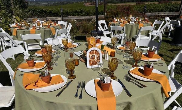 Outdoor tables set for an event with green tablecloths and orange napkins.