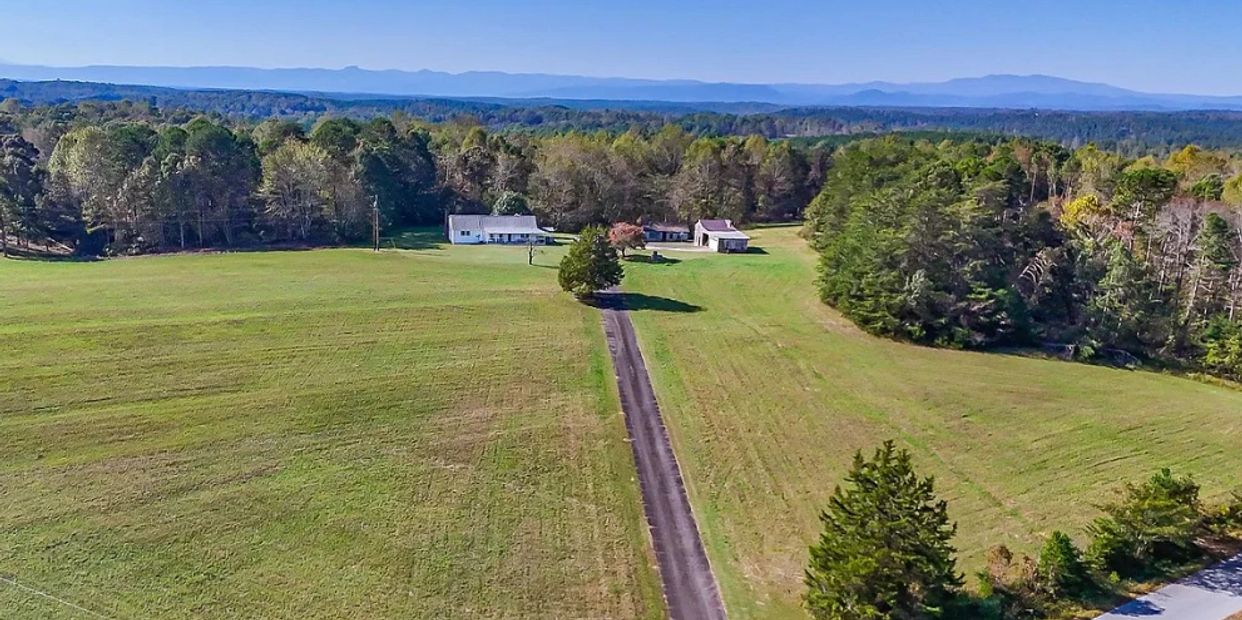 Open field with two small houses and a road.