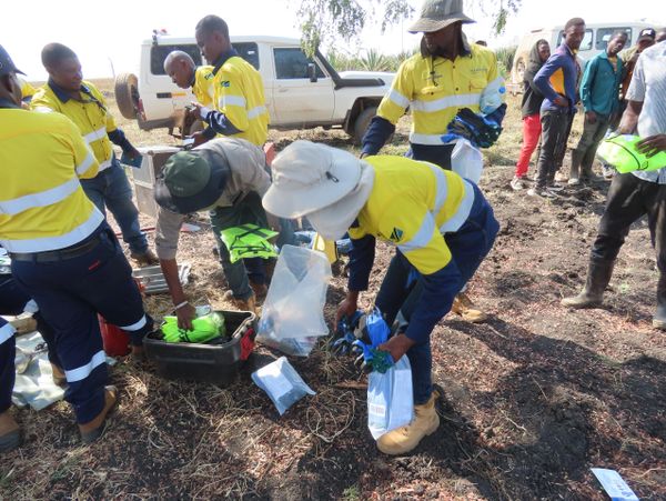 Workers in yellow safety uniforms organizing equipment outdoors.