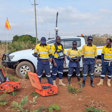 Surveyors in yellow uniforms standing near a white pickup truck with equipment cases.
