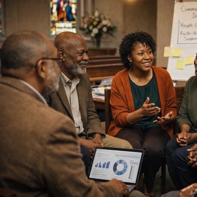 A group of diverse adults engaged in a discussion with charts on a laptop.