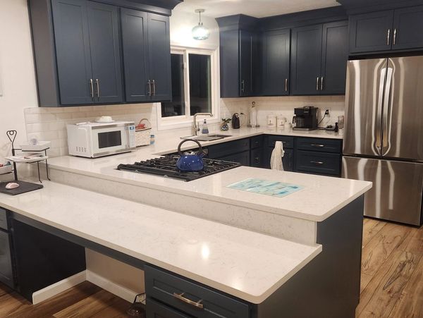 Modern kitchen with navy blue cabinets, white countertops, and wooden flooring.