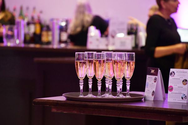 Glasses of champagne on a tray at a bar with people in the background.