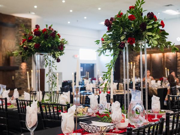 Elegant dining setup with black tablecloths, red floral centerpieces, and white napkins.