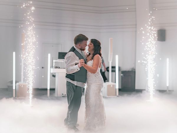Newlyweds share a joyful first dance surrounded by fog and sparkling lights.