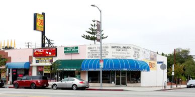 Corner storefronts with blue awnings and cars parked.