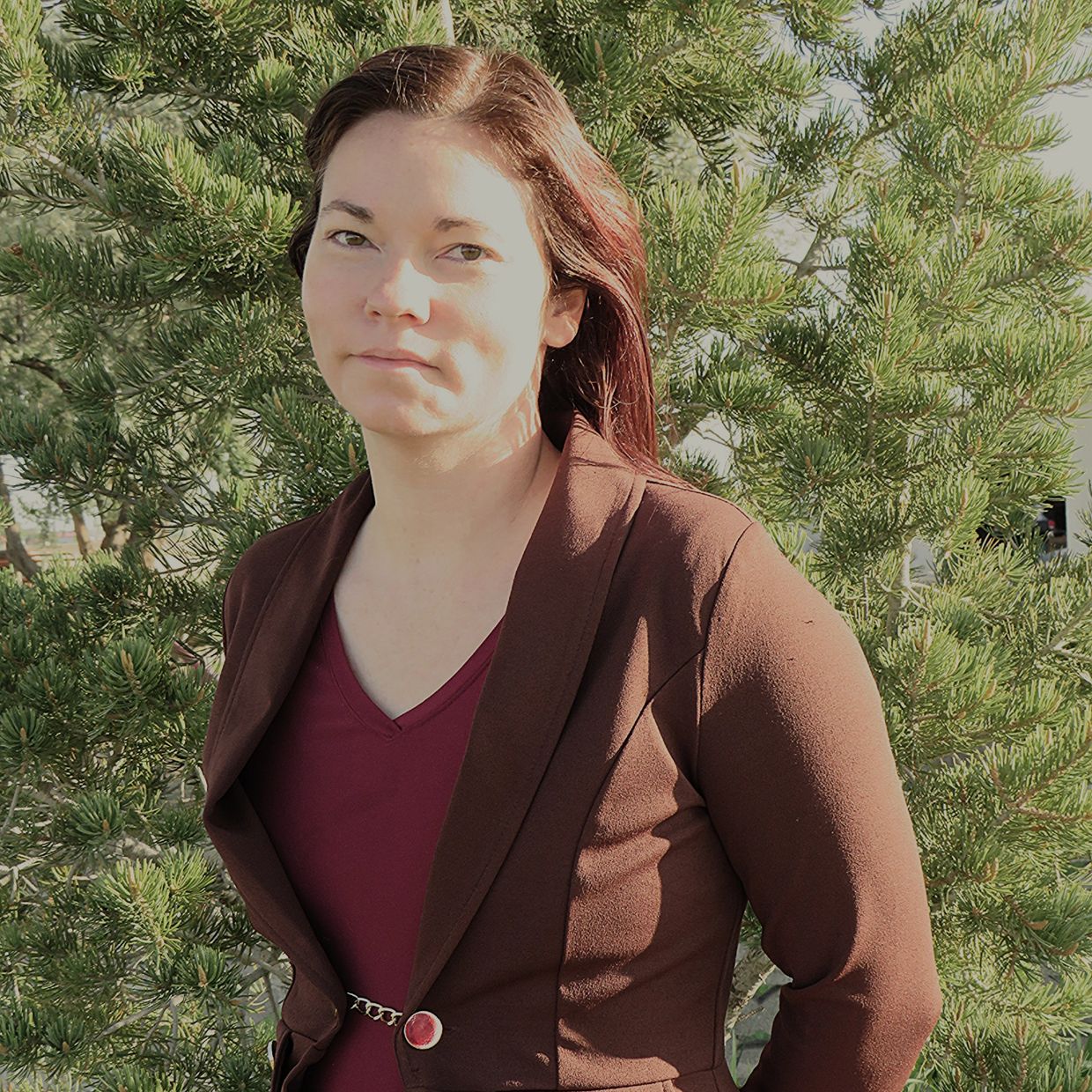 Woman in maroon top and brown jacket standing outdoors.