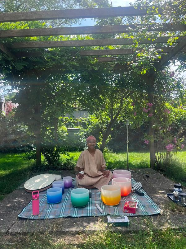 Person sitting outdoors in nature with crystal sound bowls and other sound healing instruments 