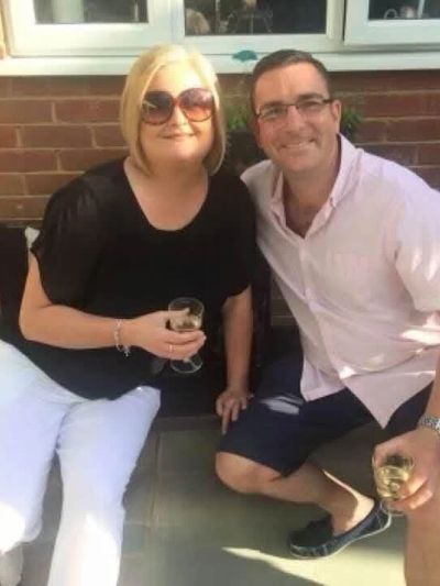 Two people smiling and holding drinks outdoors on a sunny day.