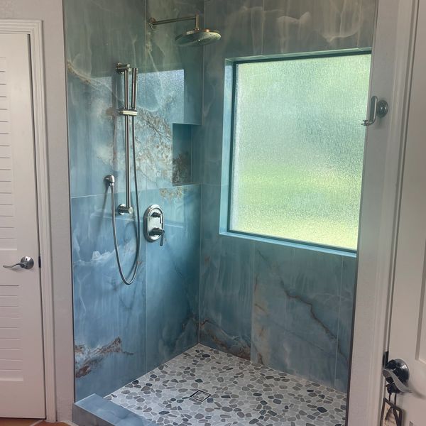 Modern shower with blue marble tiles and pebble floor.