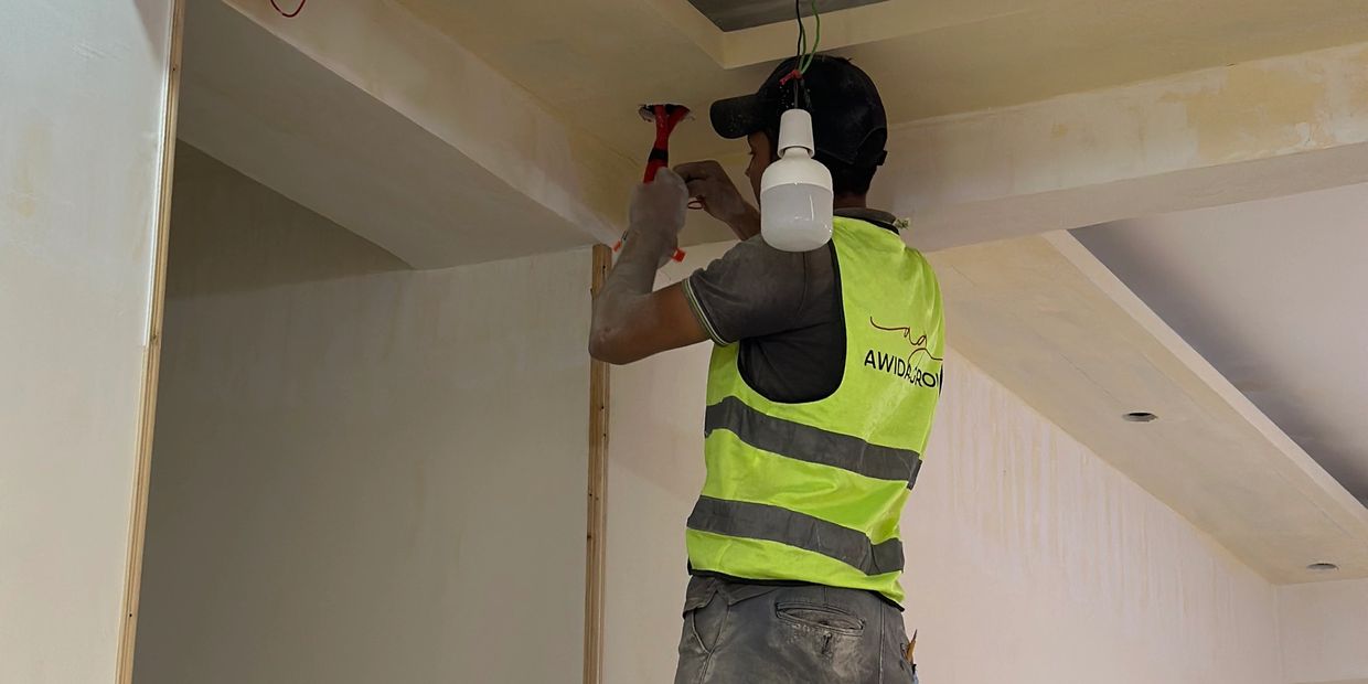 Electrician in safety vest fixing ceiling wiring with tools.