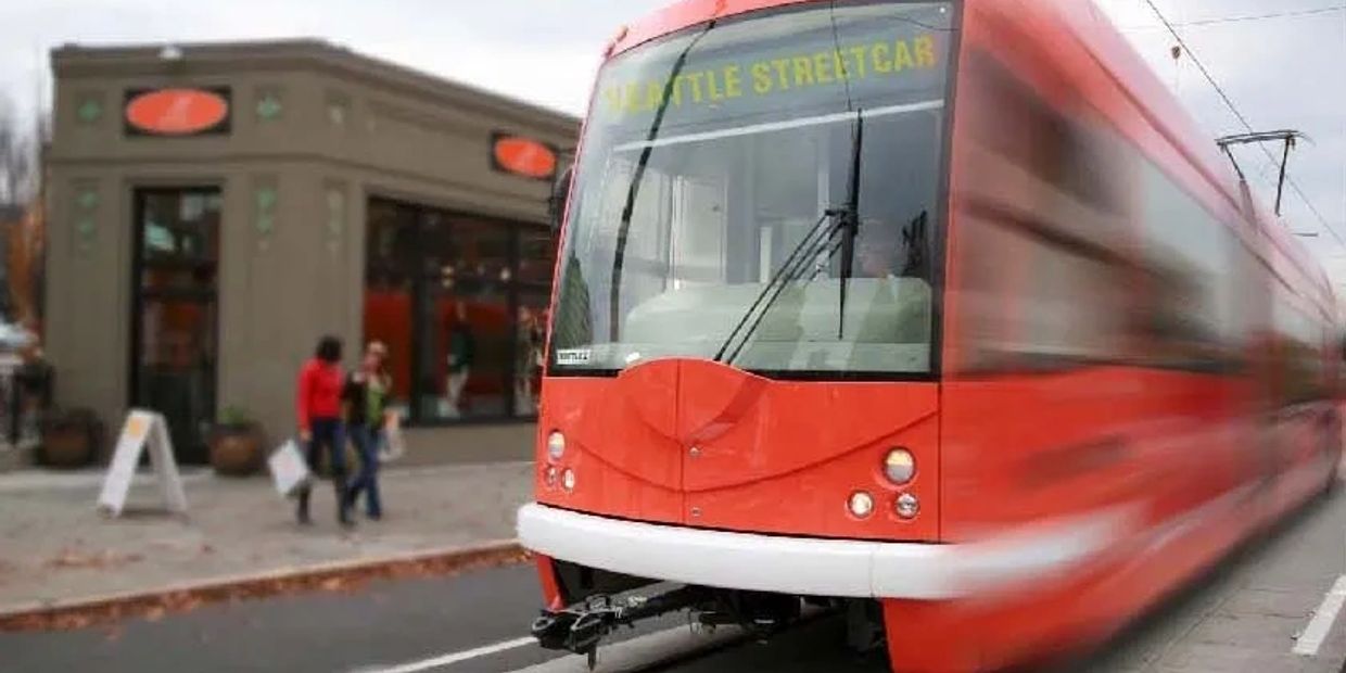A red Seattle streetcar moving on tracks beside a sidewalk.