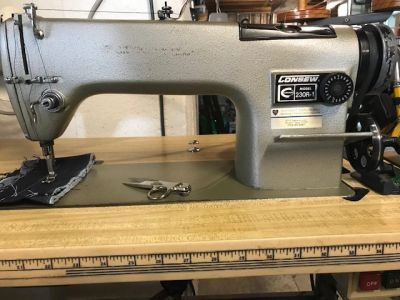 Industrial sewing machine on a wooden table with fabric and scissors.