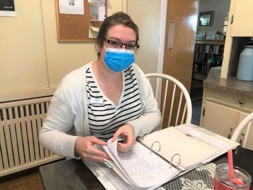 Woman wearing a mask reviewing papers at a table.