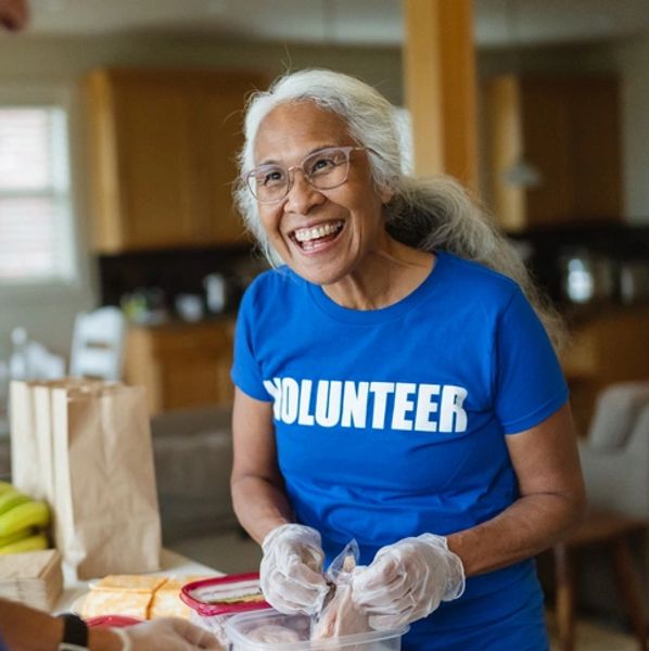 Smiling elderly woman volunteering while preparing food with gloves.