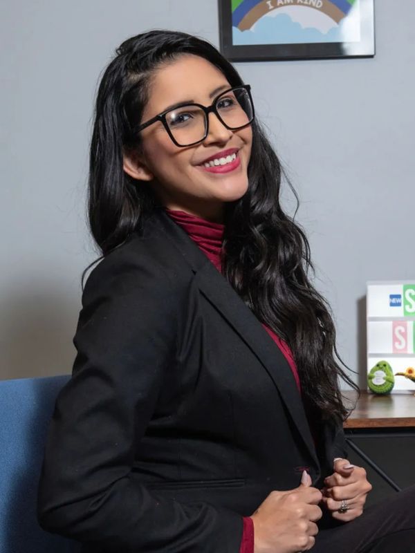 Confident woman with glasses smiling, dressed in a black blazer and maroon top.