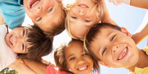 A joyful group of children smiling in a circle under the sun.