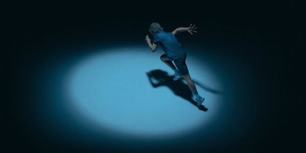 A person sprinting in a spotlight against a dark background.