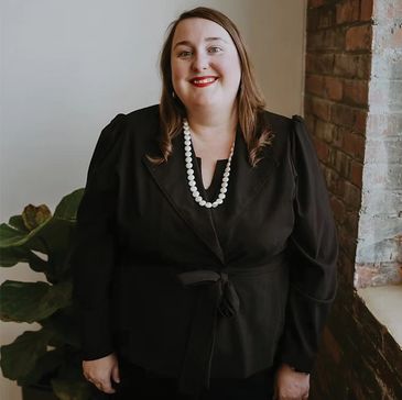 Woman in black outfit with pearl necklace smiling.